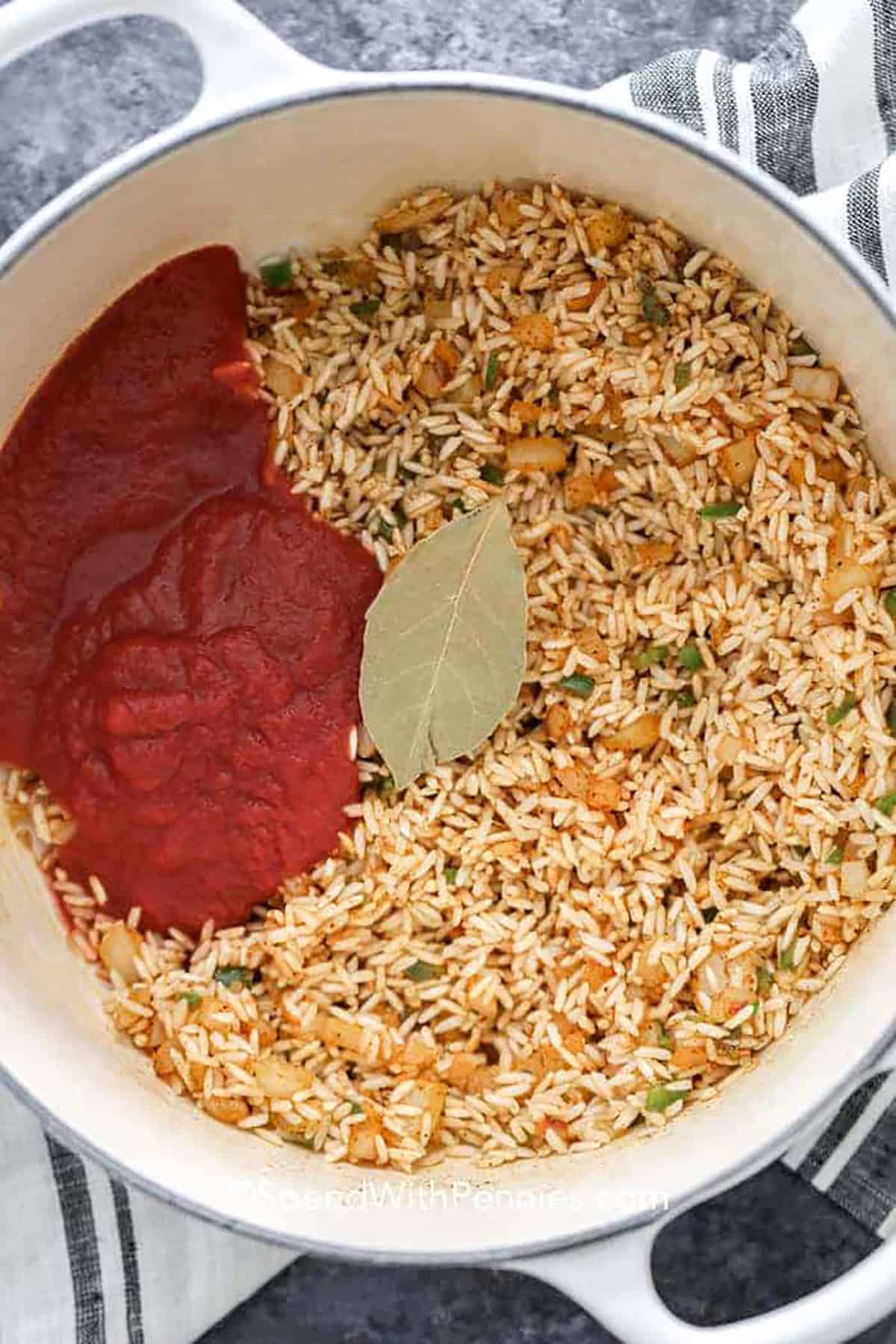 Adding tomato sauce and bay leaf to a pot to make Mexican rice.