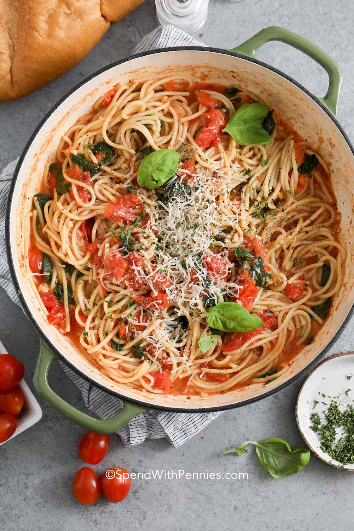 One-pot spaghetti gets an easy one-pot makeover in this fresh 30-minute dinner. Spaghetti cooks directly with cherry tomatoes, garlic, basil, and lemon zest, creating a light sauce from the flavorful starchy cooking liquid. Fresh spinach wilts in at the end, and Parmesan adds a savory, cheesy finish. Serve it on its own or pair it with salad and garlic bread. Pin this tomato spinach pasta for your next meatless dinner. #spendwithpennies One Pot Spaghetti in a pot with parmesan cheese