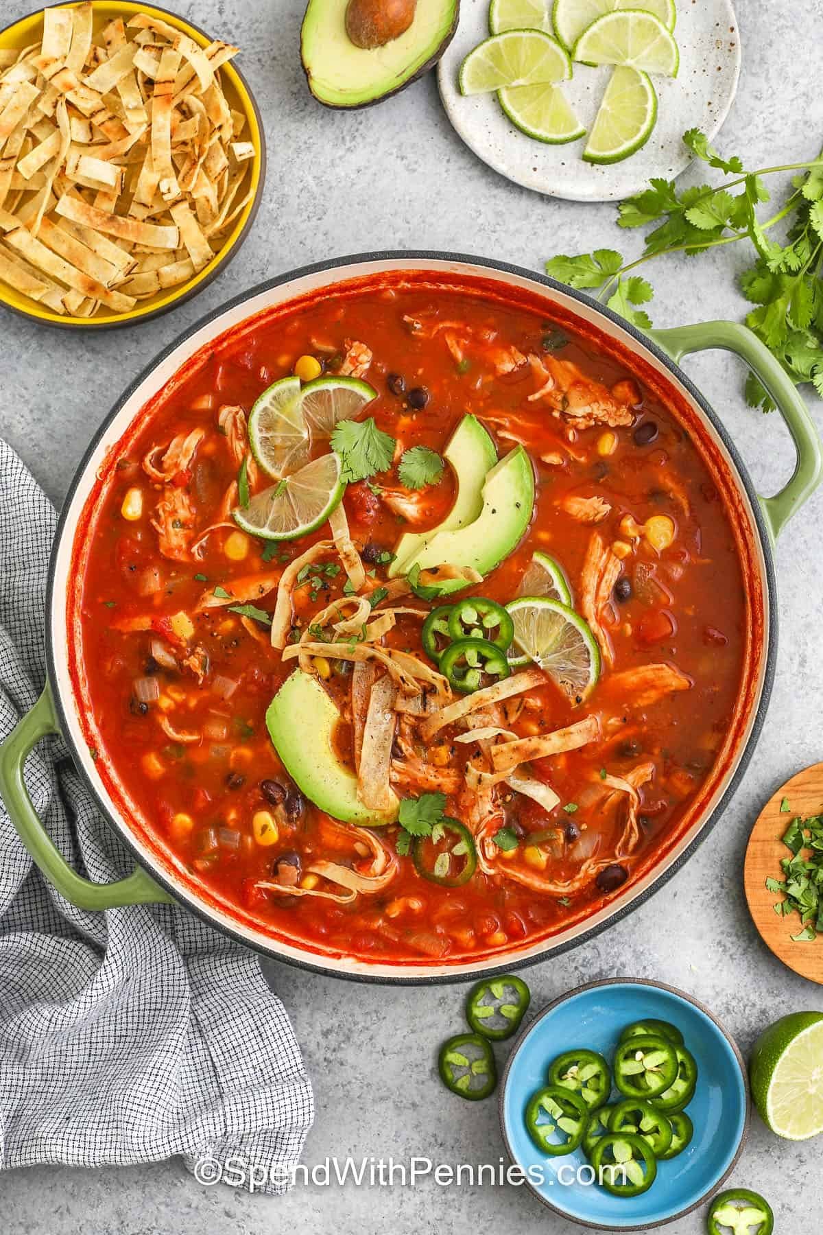 top view of chicken tortilla soup in a green serving dish and condiments