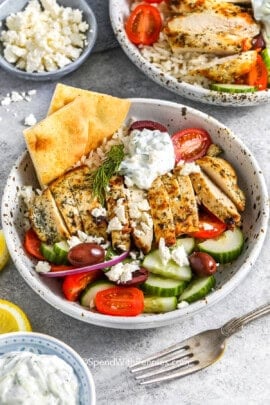 A Greek chicken bowl topped with feta cheese and served with pita