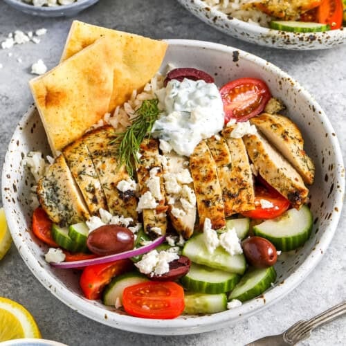 A Greek chicken bowl topped with feta cheese and served with pita