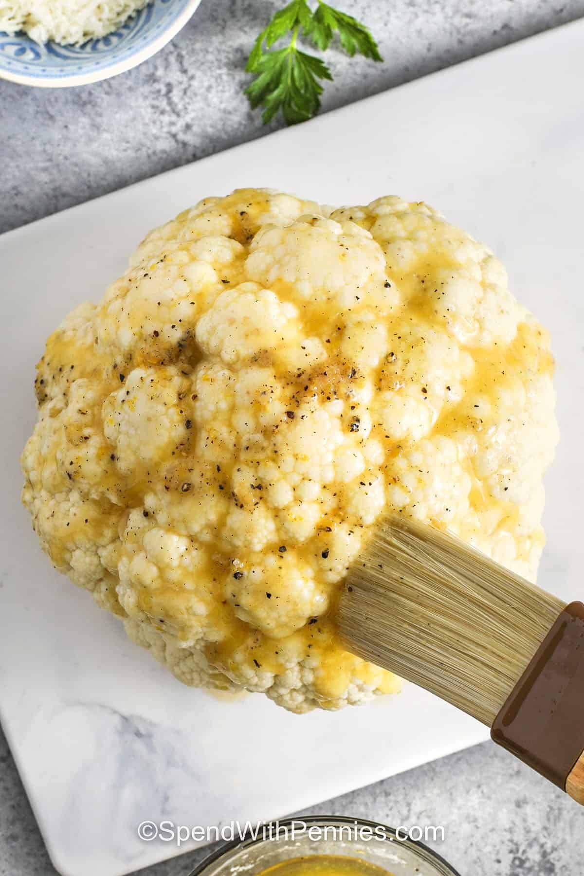 brushing a head of cauliflower with garlic butter to make whole roasted cauliflower