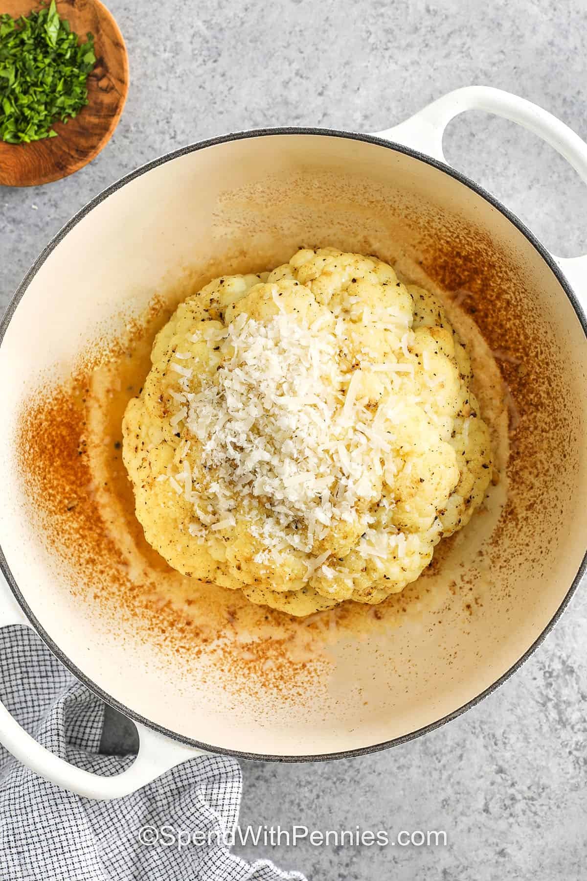 whole roasted cauliflower in a Dutch oven topped with uncooked parmesan