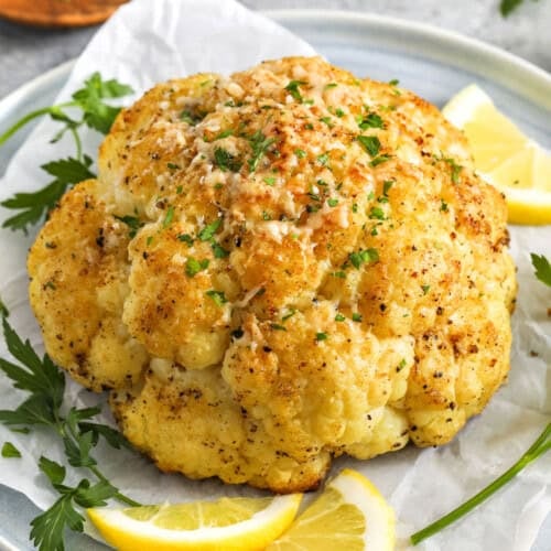plated whole roasted cauliflower with lemon slices, parmesan, and parsley in the background