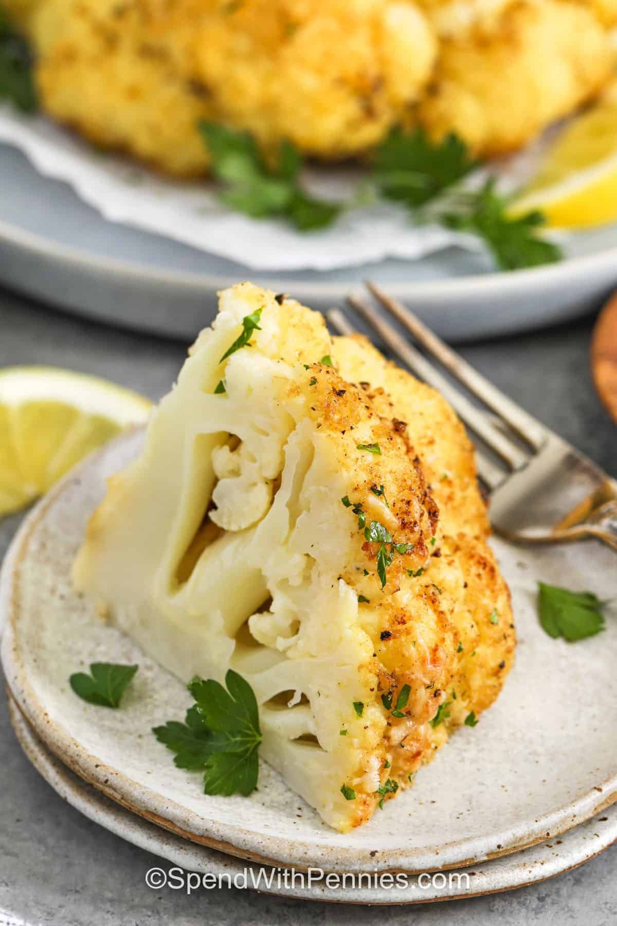 closeup of whole roasted cauliflower serving on a plate with a fork