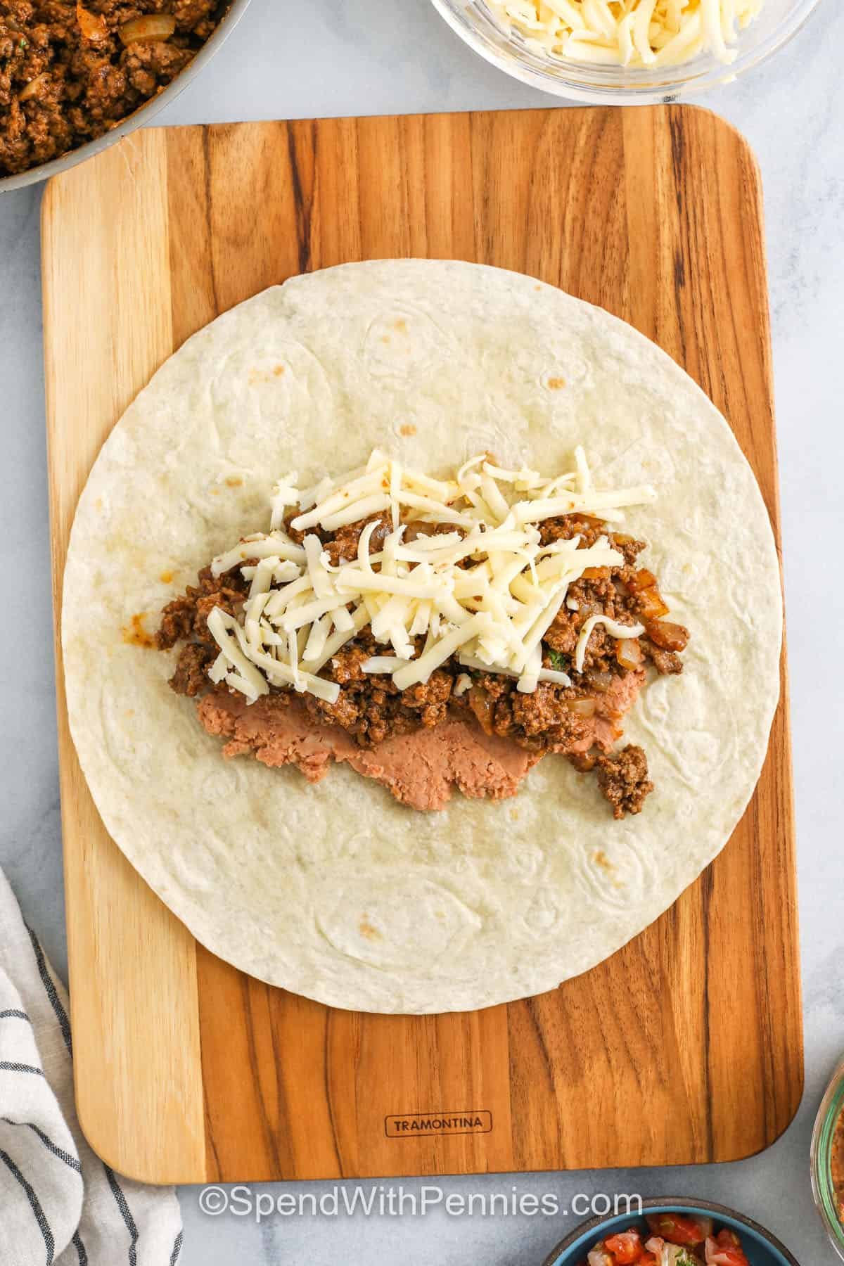 If you love big, bold flavors, this favorite beef burrito recipe is a must-try. Juicy ground beef is seasoned to perfection and paired with smooth refried beans, melty pepper jack cheese, and soft flour tortillas. Optional cilantro gives a burst of freshness, while a quick toast in the skillet brings extra crunch. These burritos are easy to make, easy to freeze, and even easier to love—great for dinner, lunch, or anytime cravings hit! #spendwithpennies adding ingredients to tortilla to make Beef Burrito Recipe