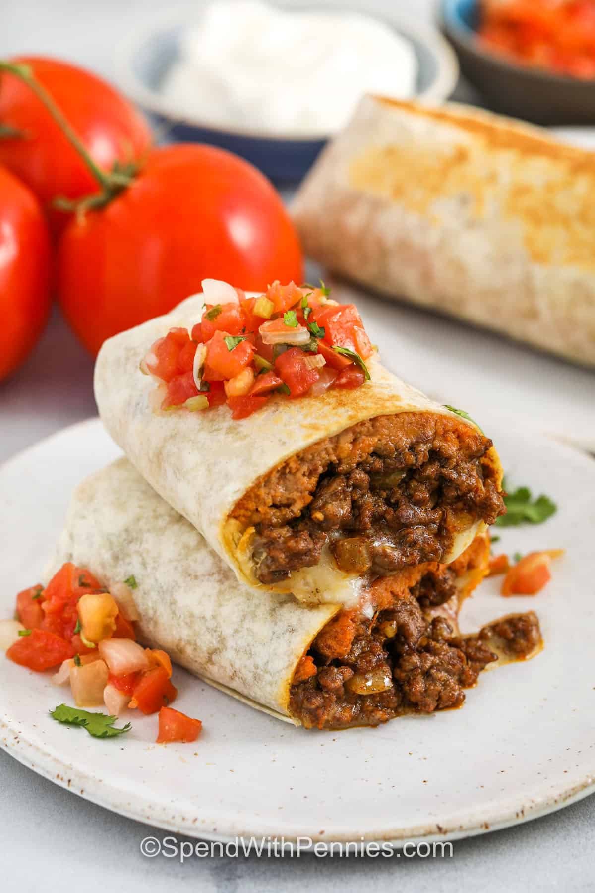 With bold flavors and a satisfying texture, this favorite beef burrito recipe is a guaranteed crowd-pleaser. It starts with seasoned ground beef and sautéed onions, layered over refried beans, then topped with shredded pepper jack cheese and wrapped in a warm flour tortilla. For added crunch and flavor, brown each burrito in a skillet before serving. Easy to customize and fun to make, this recipe is a weeknight win! #spendwithpennies plated slices of Beef Burrito Recipe