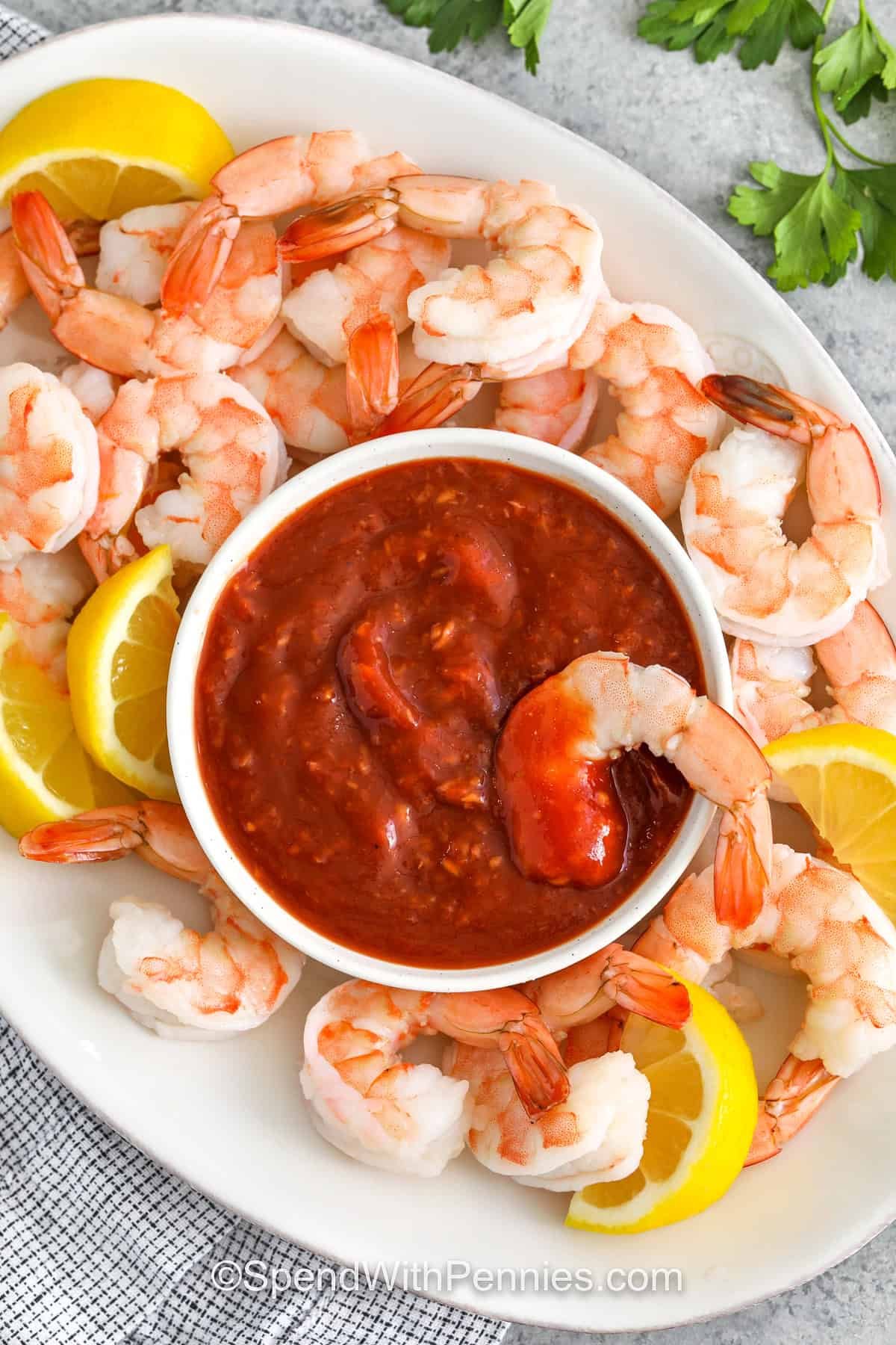 This cocktail sauce recipe is a bold and tangy favorite made with just a handful of ingredients. Ketchup and horseradish bring that sweet heat, while lemon juice and Worcestershire add a fresh, savory twist. A pinch of salt and pepper rounds it out perfectly. Chill it for 30 minutes and serve with shrimp or seafood for a flavor-packed dip. #spendwithpennies plated Cocktail Sauce with shrimp and lemon slices