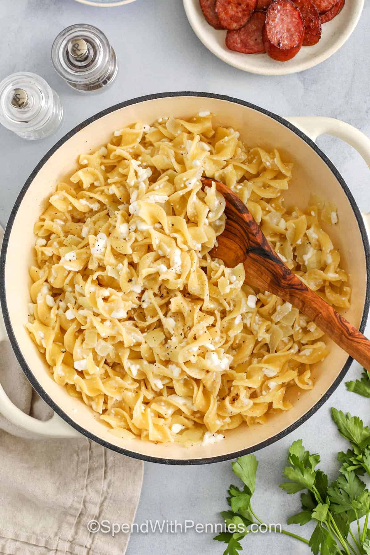 Cottage cheese and noodles are a simple dish that feels like home. This recipe blends boiled egg noodles with golden onion, rich butter, and creamy cottage cheese for a classic combo that’s big on comfort. Want to take it up a notch? Add a sprinkle of Parmesan and broil it in the oven. Don’t forget the sour cream on top for a cool, tangy finish. #spendwithpennies mixing Cottage Cheese and Noodles in the pot with a wooden spoon