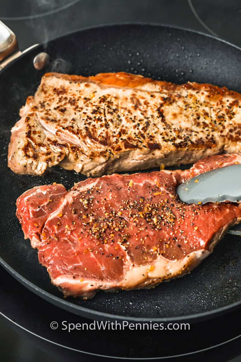 Cooking juicy steak in the oven is simple with this mouthwatering ribeye recipe. Searing locks in flavor while a quick oven finish cooks them evenly. The optional garlic herb cream sauce adds a rich, restaurant-style touch that’s ready in minutes. Serve with your favorite sides for a steakhouse dinner at home. #spendwithpennies flipping over Juicy Oven Steak in the pan