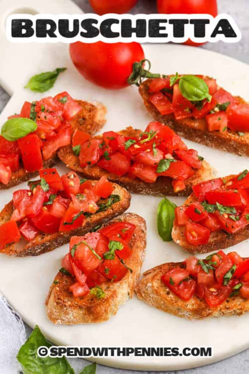 Tomato bruschetta is a flavorful and budget-friendly way to enjoy the fresh taste of summer all year long. With ripe tomatoes, aromatic basil, and minced garlic tossed in olive oil, it’s a refreshing topping for toasted baguette slices. Make the tomato mix ahead and assemble just before serving for easy entertaining. #spendwithpennies plate of Bruschetta with a title