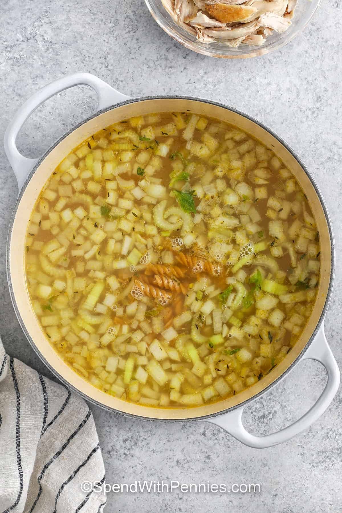 adding broth and noddles to cooked vegetables to make Rotisserie Chicken Soup