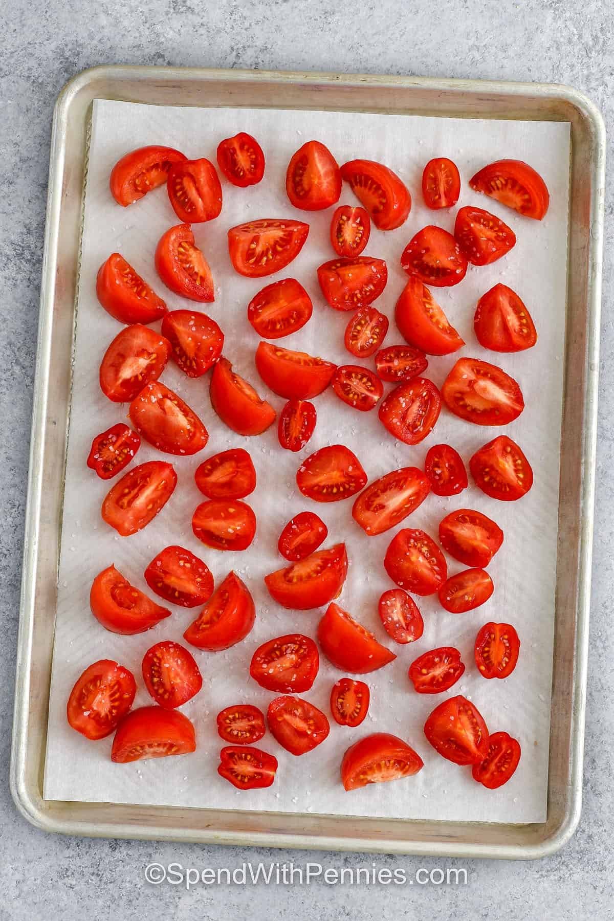 These delicious sun dried tomatoes are slow-roasted to perfection with just salt and time, letting their natural sweetness shine through. Finished with olive oil and basil, they make the perfect topping for bruschetta, pasta, or salads. Store them in a jar for easy access to rich tomato flavor at any time. This recipe is simple and versatile. So much flavor in every bite! #spendwithpennies seasoned tomatoes on a sheet pan to make Sun Dried Tomatoes