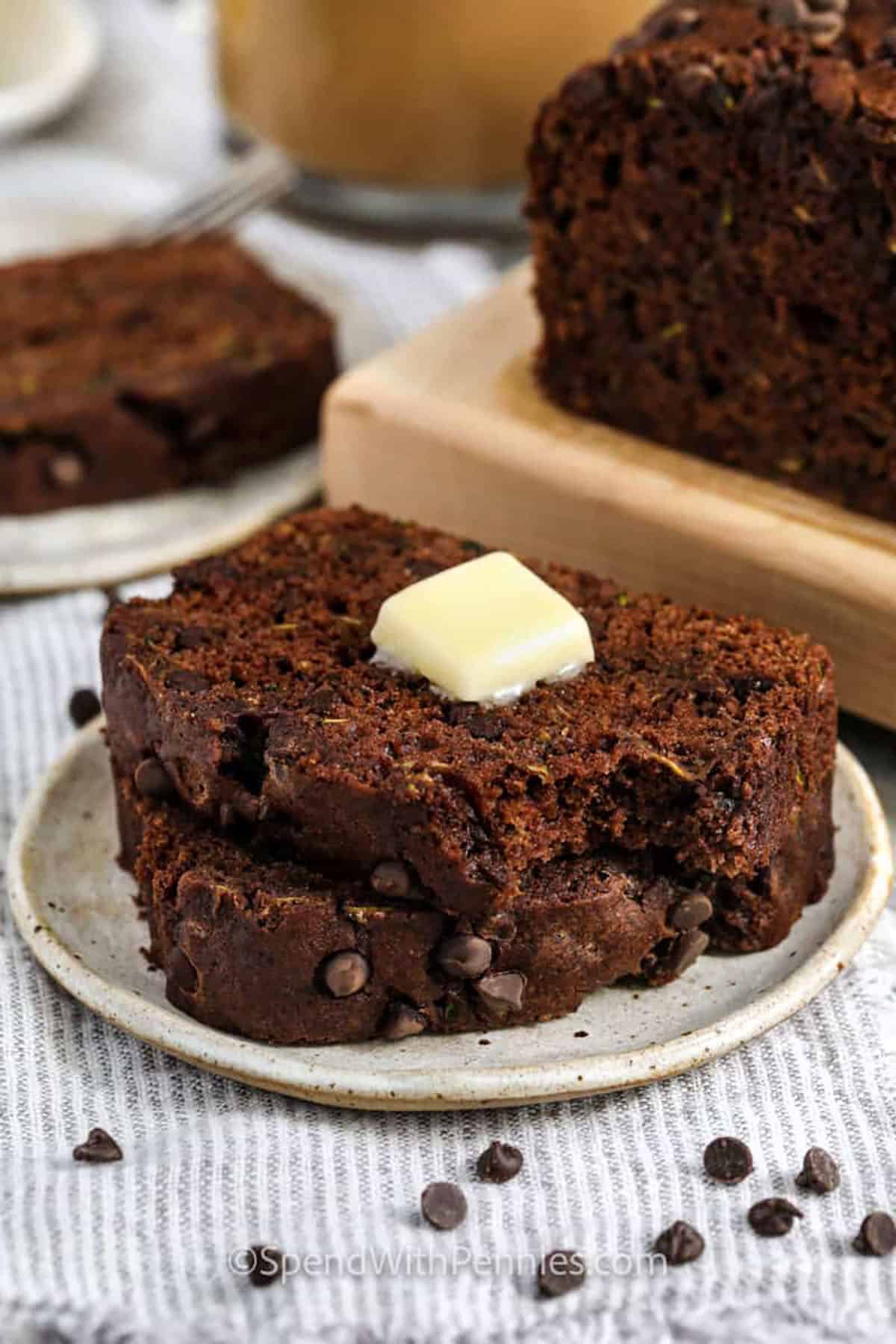 This chocolate zucchini bread recipe is the best way to use up fresh zucchini. It’s moist, rich, and packed with double chocolate flavor thanks to cocoa and mini chocolate chips. Applesauce keeps things light, so it’s a healthy treat you can feel good about. Want even more crunch? Add in some chopped almonds or walnuts for extra texture. This simple homemade loaf is one you’ll make again and again. #spendwithpennies slices of Chocolate Zucchini Bread on a plate with a bite taken out and butter on top