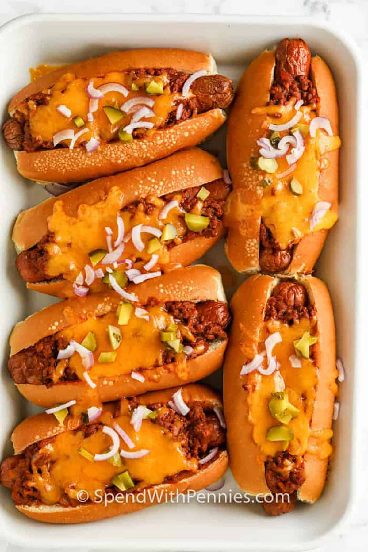 Chili cheese dogs are the baked comfort food you’ll want to make on repeat. These hot dogs are tucked into soft buns, smothered with chili, and topped with melty cheddar for the best game day or family night dinner. This hot recipe works great with homemade or leftover chili and can be loaded with all the toppings you love. For an easy meal prep idea, turn it into a chili cheese dog casserole. Everyone will be asking for seconds. #spendwithpennies plate of Chili Cheese Dogs