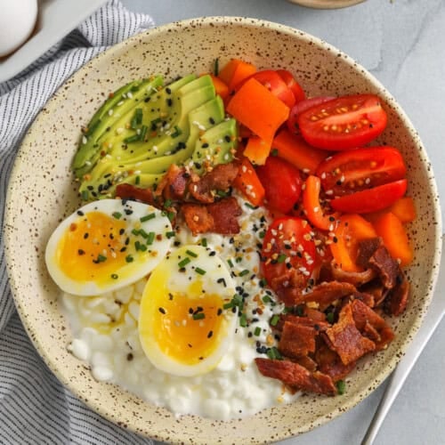 cottage cheese egg bowl in a bowl with a fork and eggs in the background