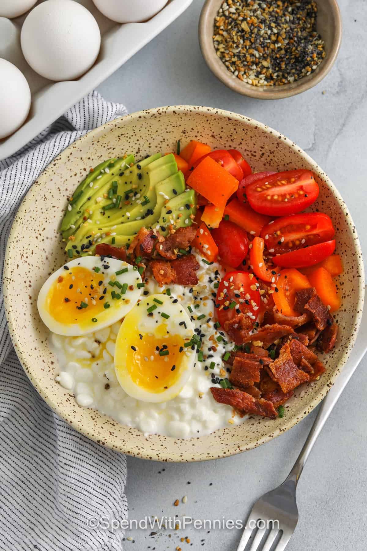 Cottage cheese breakfast bowls are a simple and healthy breakfast option loaded with protein. These bowls can be made ahead for busy mornings or enjoyed fresh. Balanced and filling, they keep you satisfied for hours. Easy, wholesome, and delicious! #spendwithpennies cottage cheese egg bowl in a bowl with a fork and eggs in the background