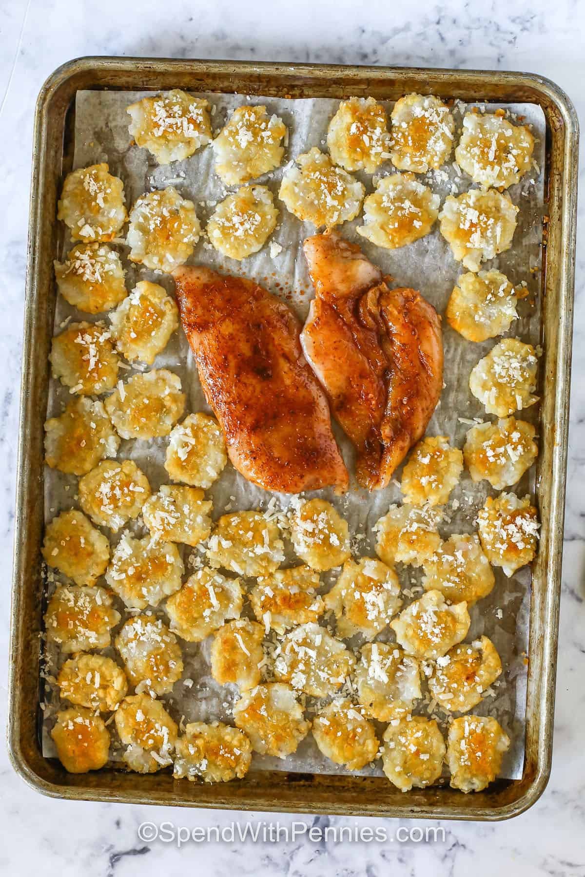 adding cheese and chicken to cooked tater tots on sheet pan to make Crispy Tater Caesar Salad