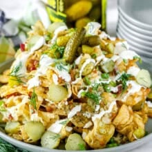 dill pickle nachos on a plate with a stack of plates and jar of pickles