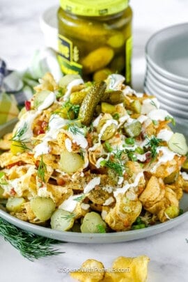 dill pickle nachos on a plate with a stack of plates and jar of pickles