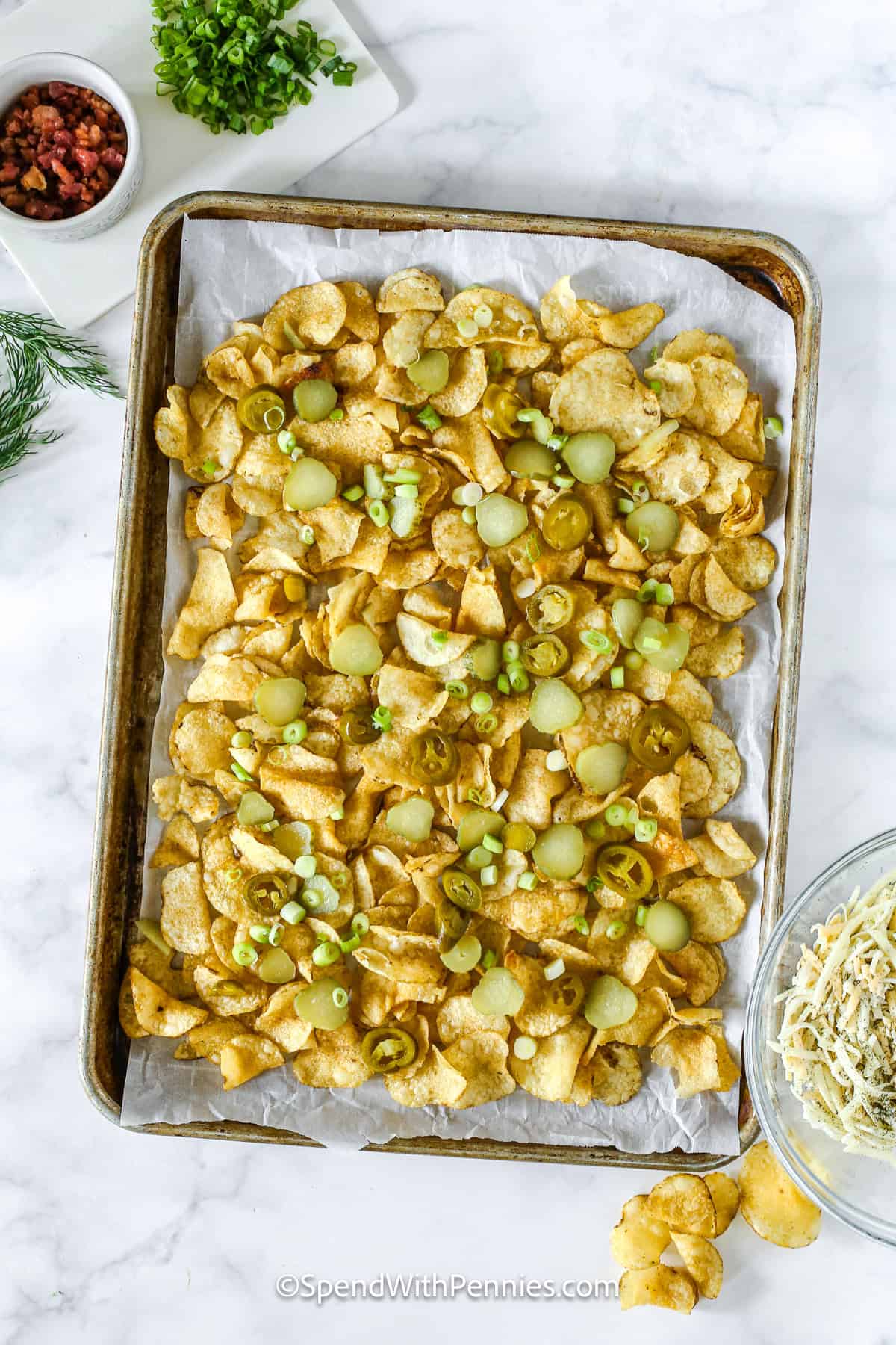 Dill pickle nachos combine crispy chips, tangy pickles, savory bacon, and gooey cheese for the perfect snack. Jalapeños and green onions add a pop of heat and freshness to every bite. Serve with a creamy dipping sauce for the ultimate flavor combo. #spendwithpennies ingredients for dill pickle nachos on a pan