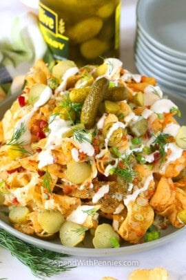 dill pickle nachos on a plate with a stack of plates and jar of pickles