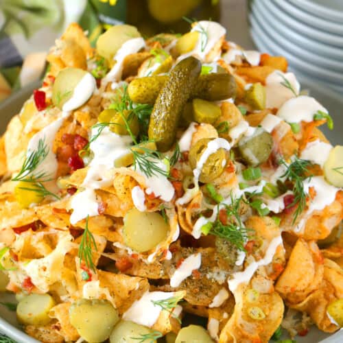 dill pickle nachos on a plate with a stack of plates and jar of pickles