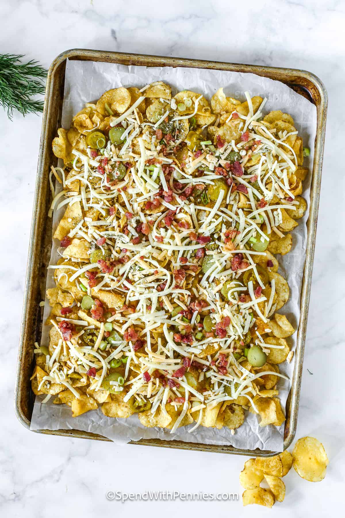 Dill pickle nachos are packed with layers of flavor from tangy pickles, crispy bacon, and melty cheese. This quick and easy recipe bakes in minutes for a snack that’s sure to please. Don’t forget the creamy sour cream and pickle juice dip on the side! #spendwithpennies cheese added to pan to make dill pickle nachos