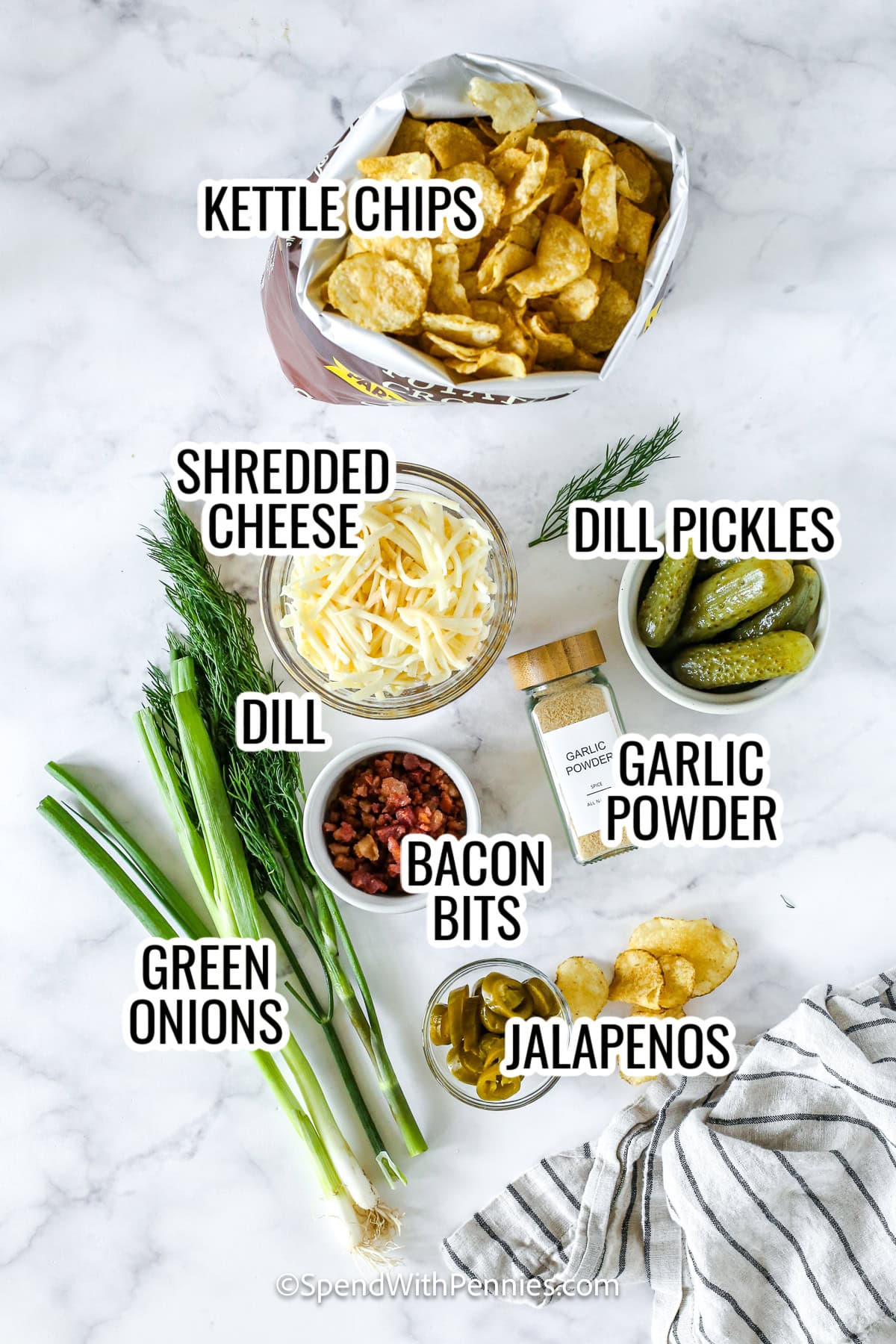 Dill pickle nachos are the ultimate crunchy, cheesy, and tangy snack for any gathering or game day. Loaded with kettle chips, melty cheese, crispy bacon, and zesty pickles, this recipe is bursting with bold flavor in every bite. The combination of pickled jalapeños and dill creates the perfect salty, savory snack. #spendwithpennies ingredients for dill pickle nachos including kettle chips, cheese, dill pickles, garlic powder, green onions, dill, bacon bits, and jalapenos