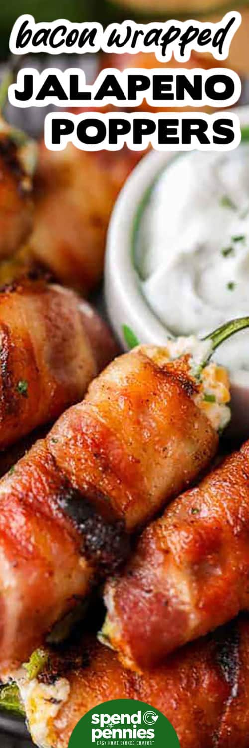 Bacon wrapped jalapeno poppers are packed with flavor, thanks to the mix of cream cheese, cheddar, garlic, and fresh green onion inside spicy jalapenos, all wrapped in crispy bacon. This recipe is easy to prep and perfect for grilling or baking, delivering a smoky, cheesy, and mildly spicy treat that everyone will love. Great for parties or casual get-togethers. #spendwithpennies close up of Bacon Wrapped Jalapeno Poppers with dip and a title