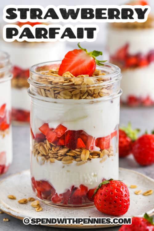 Strawberry parfaits are an easy breakfast or snack to make in minutes with just three simple ingredients. Juicy strawberries are layered with vanilla yogurt and crunchy granola in jars or glasses, ready to enjoy right away or grab and go for a mid-morning snack. This wholesome, energizing treat will keep you fueled all morning long. Vary the recipe. Try blueberry or raspberry, or make it a dessert by layering chocolate pudding or jello with whipped cream.#spendwithpennies Strawberry Parfait in a jar with a title