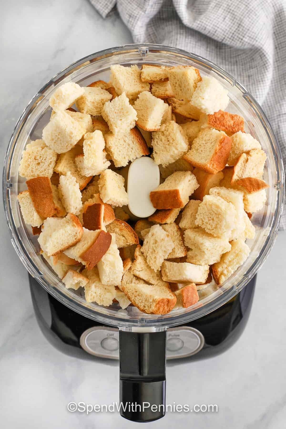 Seasoned bread crumbs add the perfect finishing touch to so many dishes, from baked mac and cheese to crispy pork chops. This easy recipe uses garlic powder, onion powder, dried herbs, and salt to create a well-balanced flavor. Use panko for extra crunch or plain for a smoother texture. They're ideal for topping casseroles or mixing into meat mixtures. Homemade and freezer-friendly for convenience! #spendwithpennies adding pieces of bread to food processor to make Seasoned Bread Crumbs