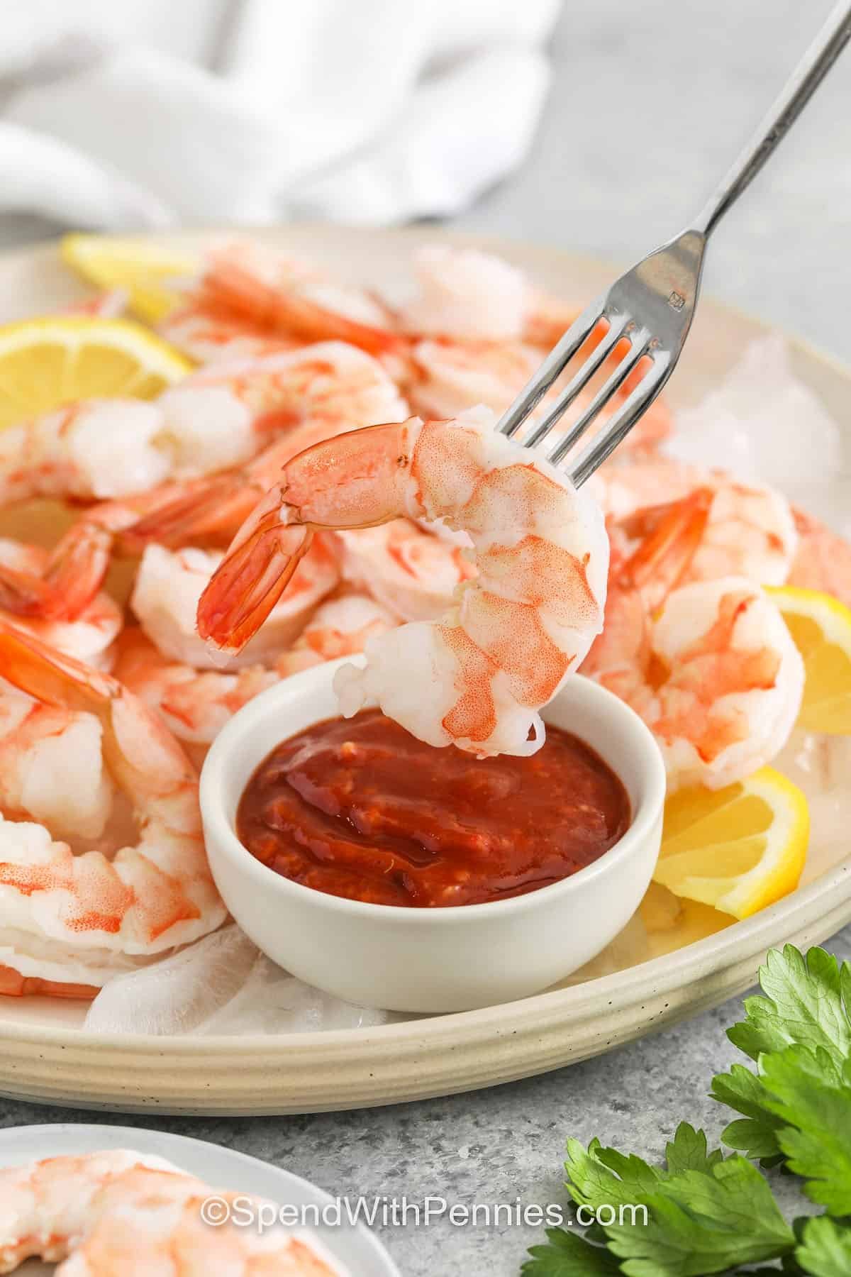 Shrimp cocktail brings bright, zesty flavor and an easy prep with this go-to party recipe. Jumbo shrimp are gently boiled with lemon and herbs, then chilled to keep the texture perfect. They’re served with cocktail sauce for dipping; just the way you want them. Great for holidays or gatherings, this is a classic you’ll want to make again and again. #spendwithpennies plated Shrimp Cocktail with dip and lemon slices