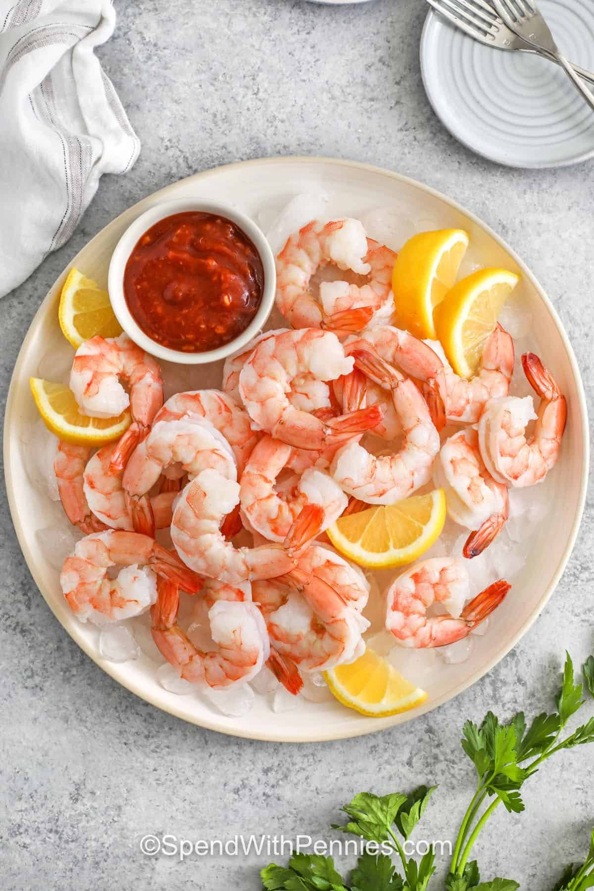 Shrimp cocktail is easy to make and tastes so much better than pre-packaged or frozen options. A quick simmer in lemon-herb water enhances flavor while keeping the shrimp juicy. Serve chilled with your favorite sauce for dipping—or let guests eat as-is for a light, refreshing bite. This simple recipe is the best way to cook shrimp for entertaining. #spendwithpennies plated Shrimp Cocktail with sauce