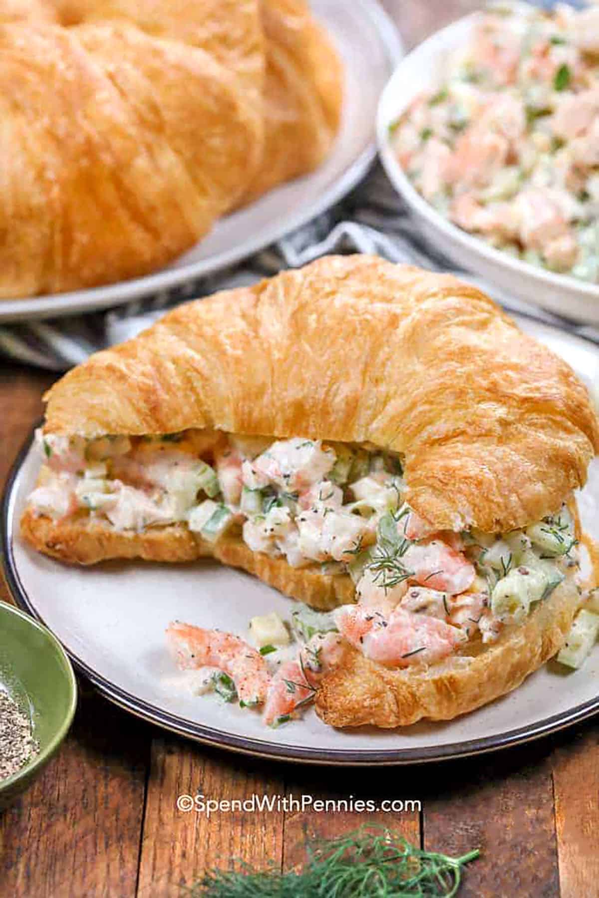 This shrimp salad recipe is a creamy mix of tender shrimp, crisp veggies, and zesty flavor. With chopped hard-boiled eggs, celery, and fresh dill, it’s loaded with texture and taste. A squeeze of lemon and dash of Old Bay make it pop. Serve it on its own, with crackers, or tucked into a croissant for a fresh and easy meal everyone will love. #spendwithpennies Shrimp Salad croissant sandwich on a plate