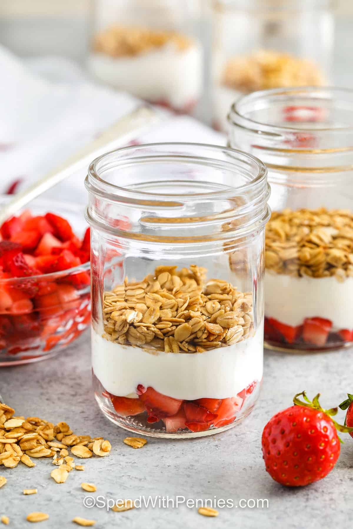 Strawberry parfait is a fresh and fun way to enjoy yogurt, fruit, and granola together. This easy recipe makes a great breakfast or snack with just a few ingredients. Add blueberries, mix in jello, or make it richer with chocolate or cheesecake layers. For a dessert-style twist, top it with whipped cream and shortcake crumbles. #spendwithpennies adding Strawberry Parfait layers to jars