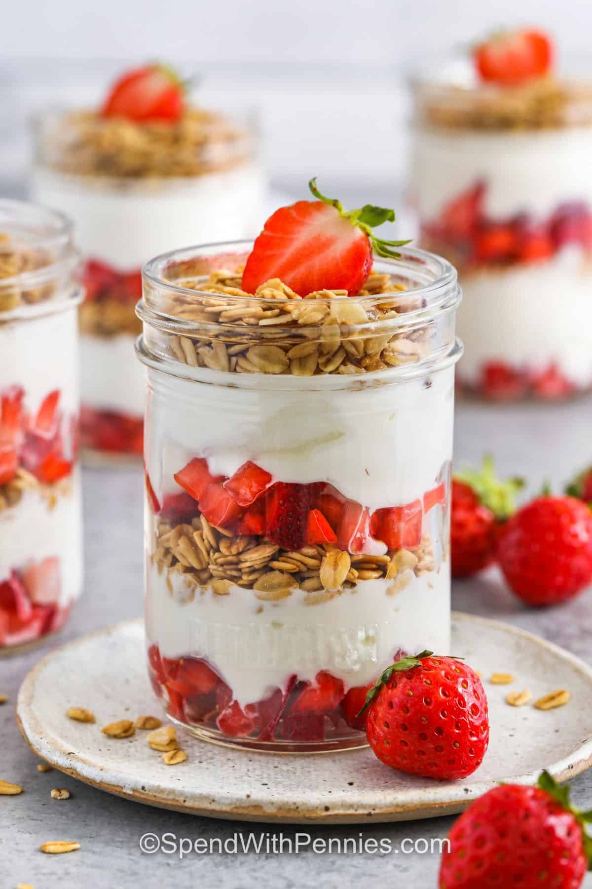 Strawberry parfait is a sweet and simple recipe you can make in minutes with yogurt, granola, and fresh berries. Layer creamy vanilla yogurt with juicy strawberries and crunchy granola for a tasty treat. Swap in blueberries or try a fun twist with cheesecake or chocolate layers. It's great for breakfast, low in calories, or dress it up with jello and cream for dessert. #spendwithpennies jars of Strawberry Parfait with one on a plate