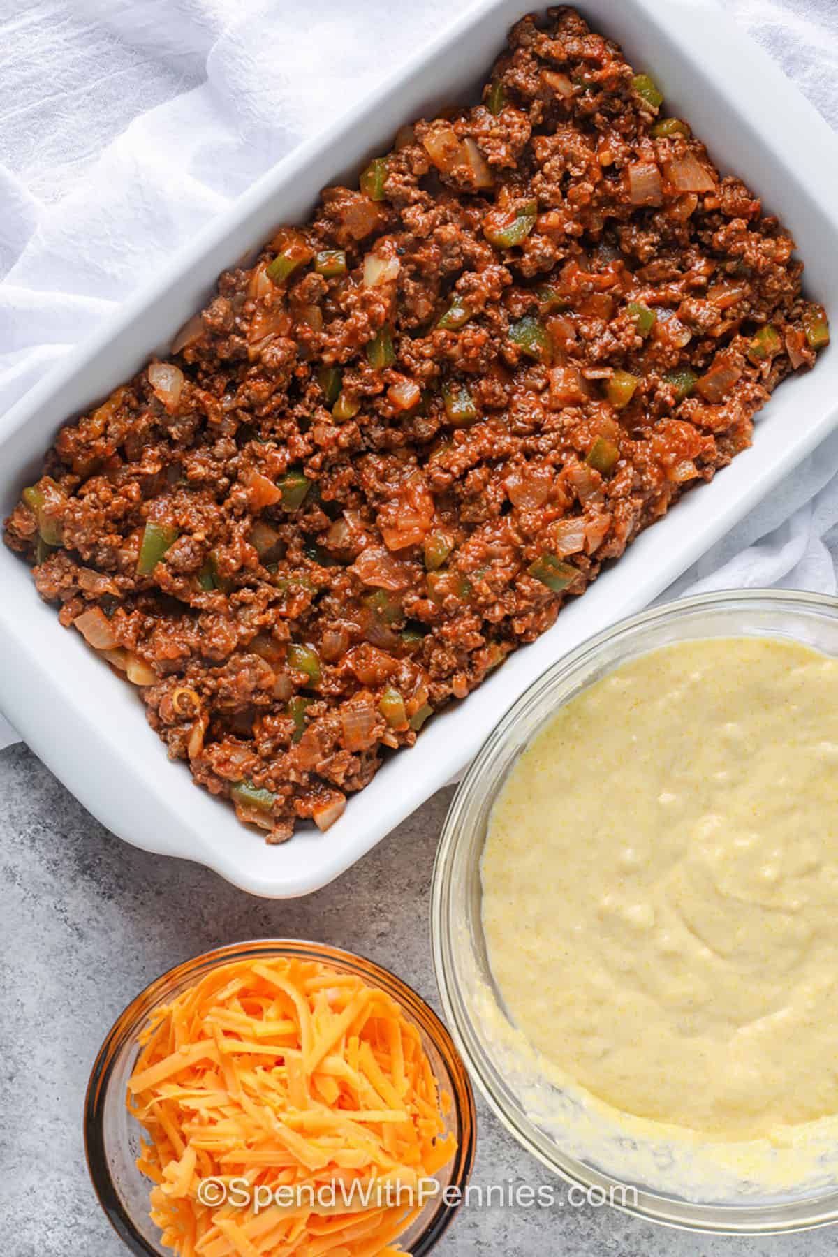 Tamale pie is the ultimate cozy dinner with layers of hearty filling and tender cornbread topping. The seasoned meat and veggie mixture is packed with flavor, while the topping adds a soft, slightly sweet contrast. Perfect for serving straight from the oven, it’s a crowd-pleaser every time. Great for make-ahead meals and casual gatherings. #spendwithpennies adding meat mixture to dish to make Tamale Pie