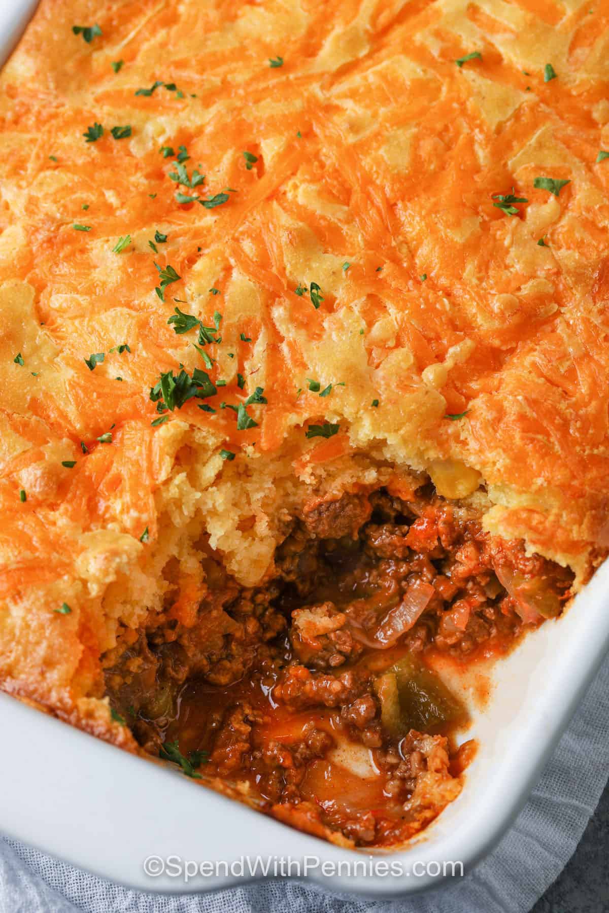 Tamale pie combines the bold flavors of seasoned beef, onions, and peppers with a tender cornbread crust. The rich filling is simmered in savory spices and sauce, making every bite warm and satisfying. This one-pan wonder is perfect for potlucks, weeknight dinners, or meal prepping ahead of time. It’s comfort food the whole family will enjoy. #spendwithpennies Tamale Pie in a dish with a portion taken out