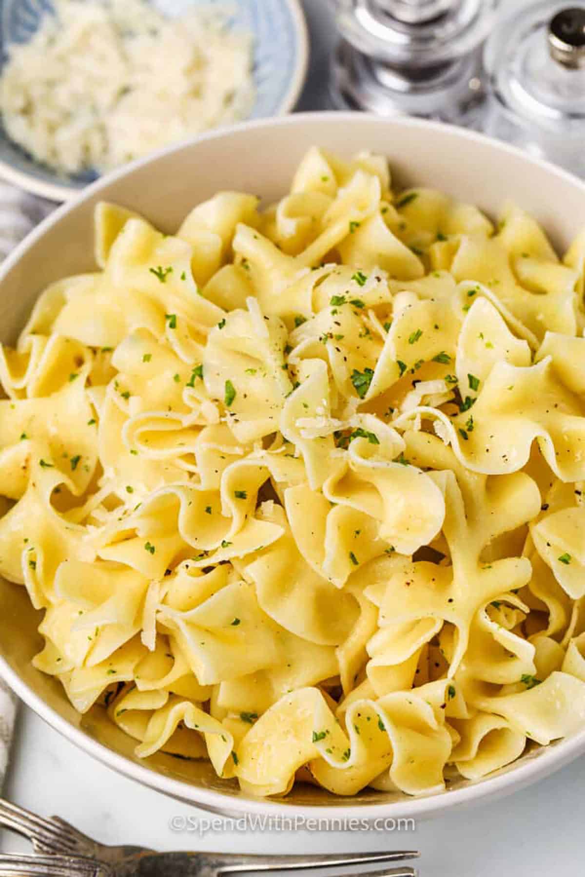 Buttered noodles bring simple, homemade comfort to the table in minutes. Delicious egg pasta is tossed in buttery goodness with garlic and fresh parsley for flavor. Add a sprinkle of Parmesan if you like it cheesy. Quick to make on the stovetop and easy to season, this is one of the best side dishes for everything from roasts to grilled chicken. #spendwithpennies bowl of Buttered Noodles with parmesan