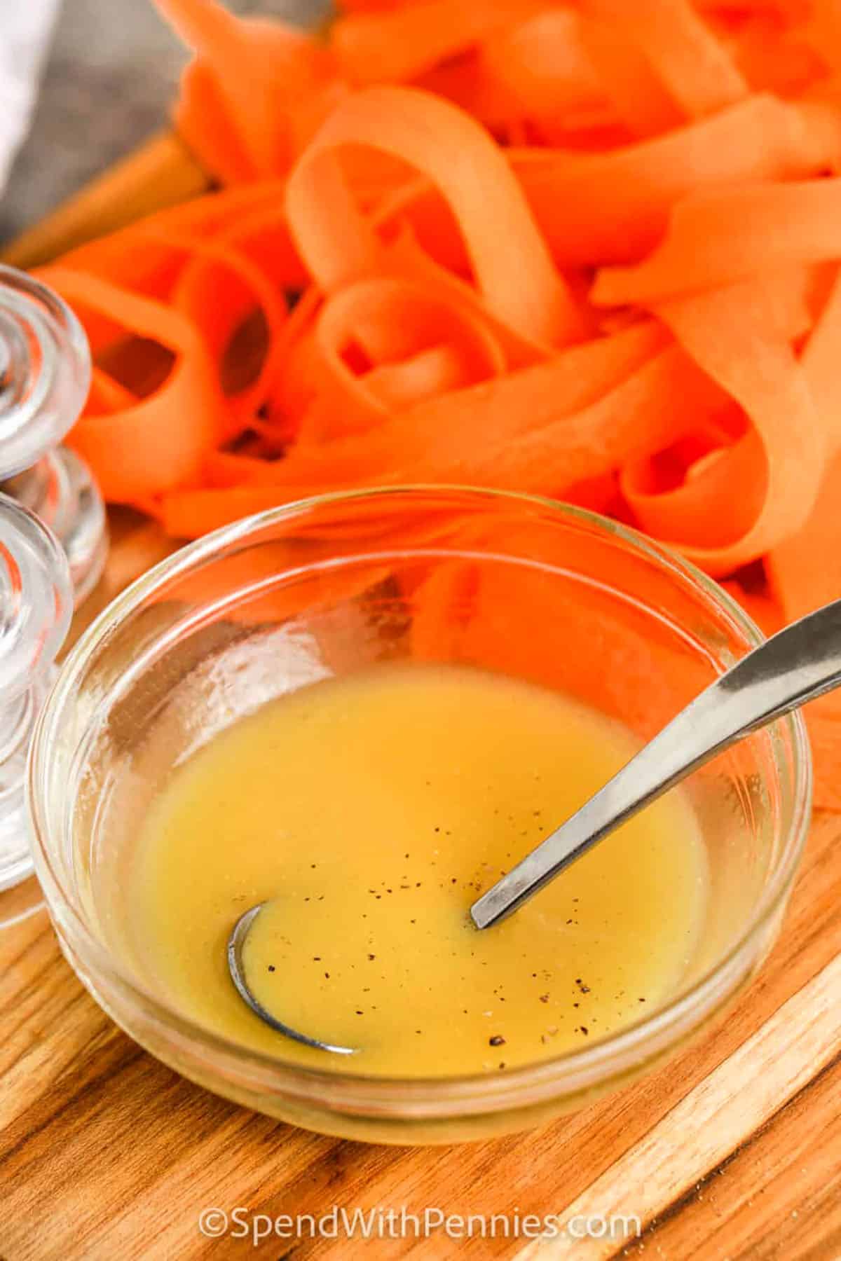 Carrot salad is the perfect mix of crisp, light, and zesty flavors. Fresh carrots, peeled into ribbons or shredded, are tossed in a tangy lemon and honey dressing that’s both simple and delicious. A sprinkle of parsley and dill gives it a bright herb finish that makes it taste so refreshing. Served cold, it’s an easy dish that works well as a side or can be made into a meal with added protein. #spendwithpennies ribbon carrots and sauce in dish to make Herbed Carrot Salad