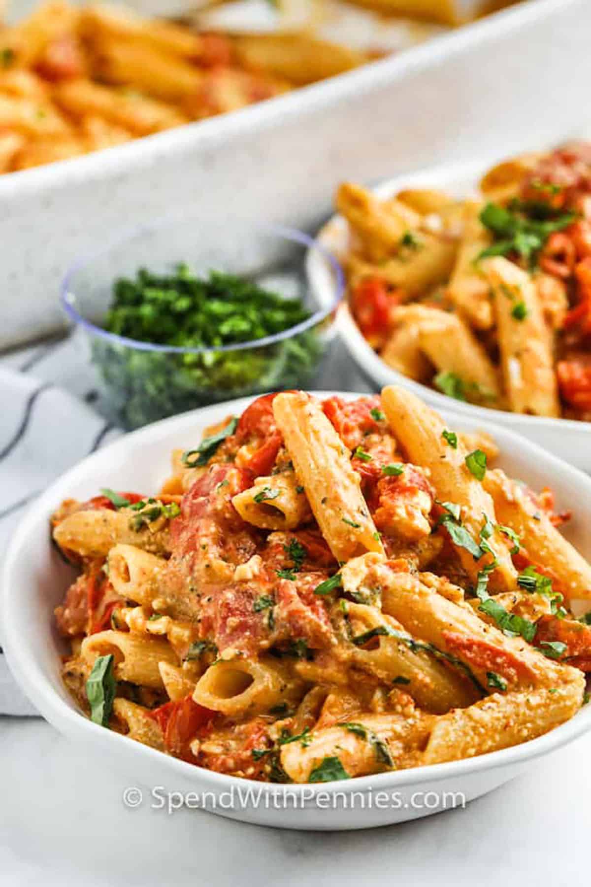 Baked feta pasta is a creamy tomato recipe that brings bold flavor to the table with ease. The oven bakes garlic, cherry tomatoes, and a block of cheese until everything is soft, bubbling, and ready to stir. This one-pan dish becomes a silky sauce that clings to pasta in the most delicious way. Roasted flavors, creamy cheese, and fresh herbs make this baked vegetarian dish a favorite for everyone at the table. #spendwithpennies bowls of Baked Feta Pasta