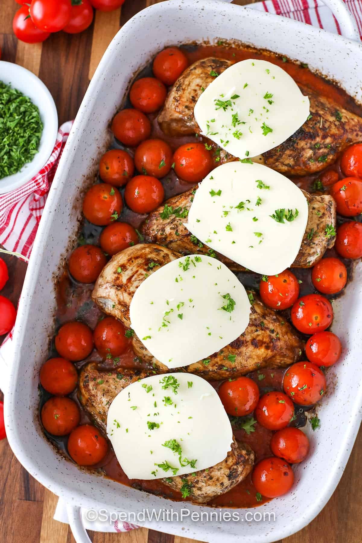 Bruschetta chicken is a baked casserole dish that’s loaded with Italian flavors. Tender chicken breast rests on marinara with cherry tomatoes, mozzarella, and a tangy balsamic drizzle. A fresh tomato and basil topping adds the perfect finish. This easy recipe is delicious over pasta, with garlic bread, or alongside a crisp green salad. #spendwithpennies adding cheese to Bruschetta Chicken in dish