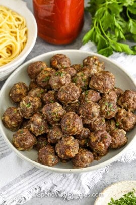 bowl of Easy Meatball Recipe with a bowl of spaghetti and jar of spaghetti sauce behind