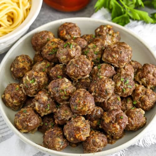 bowl of Easy Meatball Recipe with a bowl of spaghetti and jar of spaghetti sauce behind