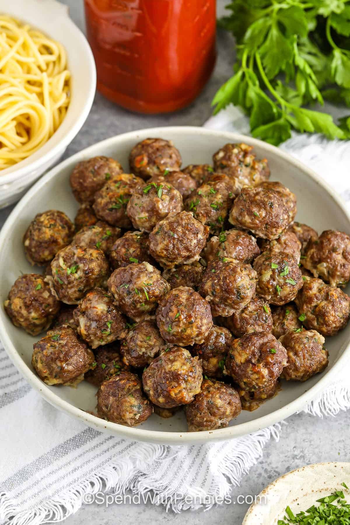 bowl of Easy Meatball Recipe with a bowl of spaghetti and jar of spaghetti sauce behind