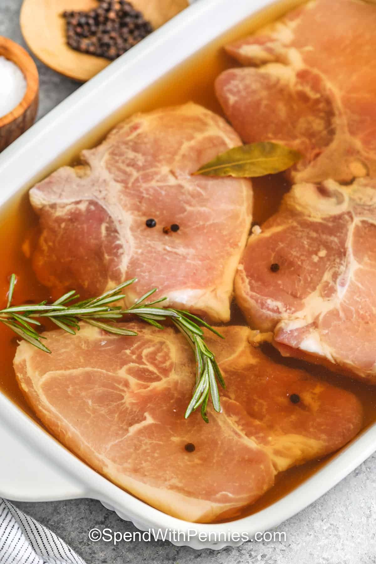 This pork chop brine makes pork taste amazing with very little work. Salt and sugar balance each other while herbs add a touch of freshness, creating pork that is seasoned and tender in every bite. The chops come out juicy and flavorful, ready to pair with any sides you like. It’s such an easy way to make dinner feel special without adding a lot of extra steps in the kitchen. #spendwithpennies close up of pork chop marinading to make Pork Chop Brine