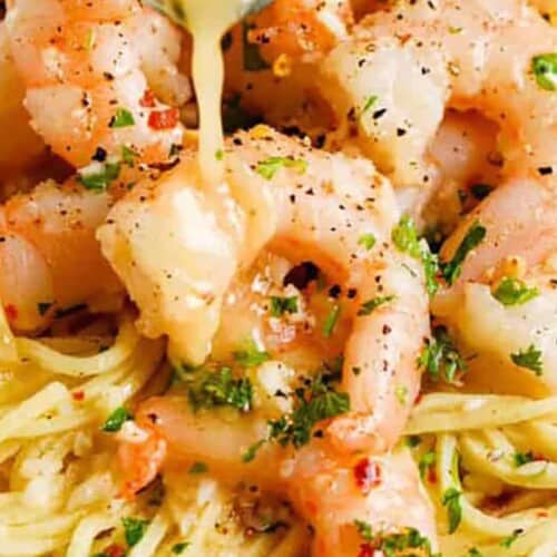 cooked shrimp scampi with a lemon slice and butter served over spaghetti
