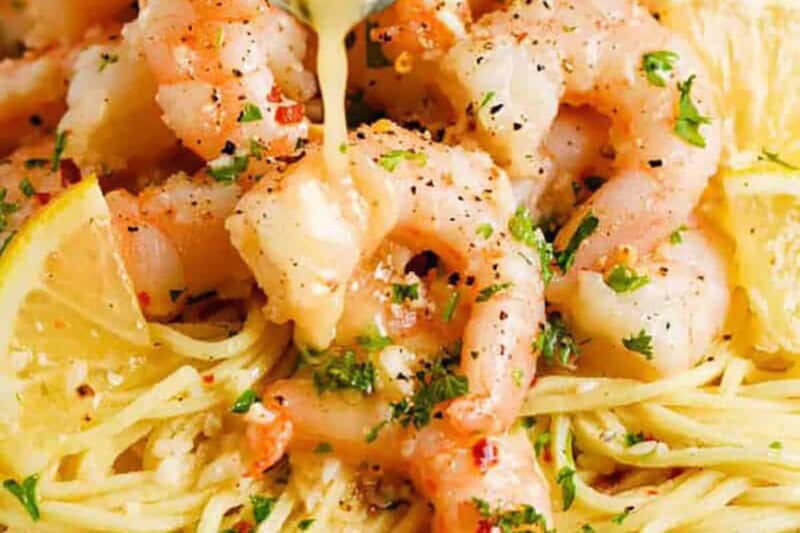 cooked shrimp scampi with a lemon slice and butter served over spaghetti