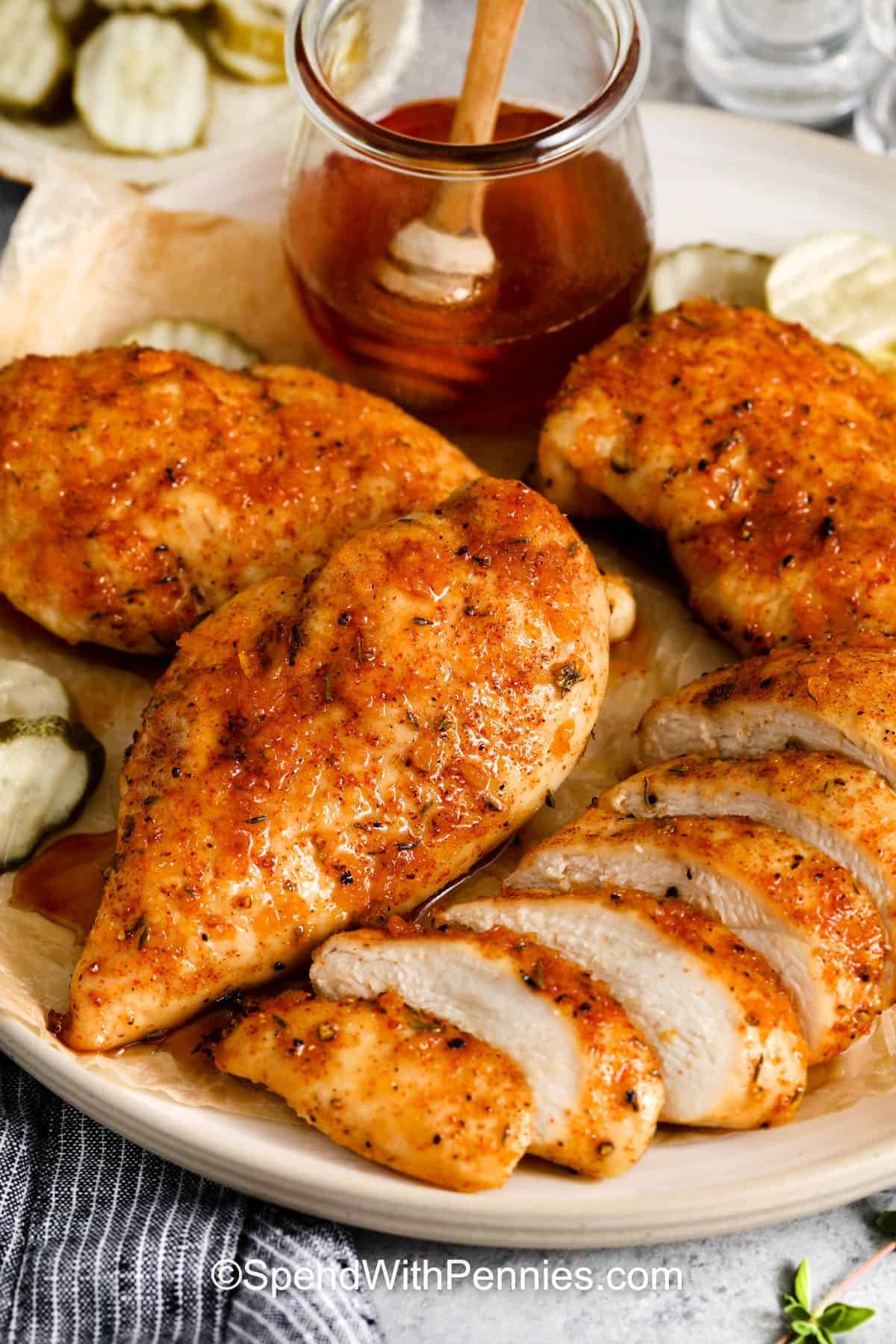 Hot honey chicken is a recipe that balances sweet, spicy, and savory flavors. Chicken breasts are seasoned and baked, then glazed with a buttery hot honey sauce infused with garlic and vinegar. Serve the chicken whole, slice it into tenders, or add it to a sandwich for a flavorful twist. This dish is perfect with roasted veggies, a fresh salad, or a simple grain bowl. #spendwithpennies plated Hot Honey Chicken with a jar of hot honey